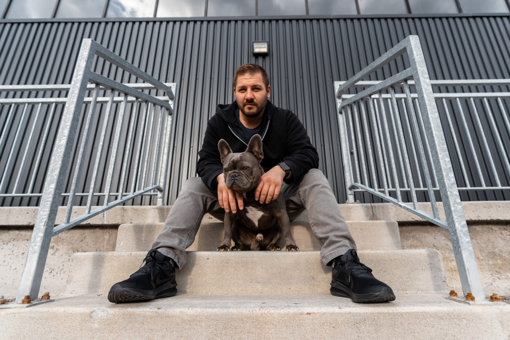 Peter K sitting on a set of stairs with his blue french bulldog playing being the alpha of the pack